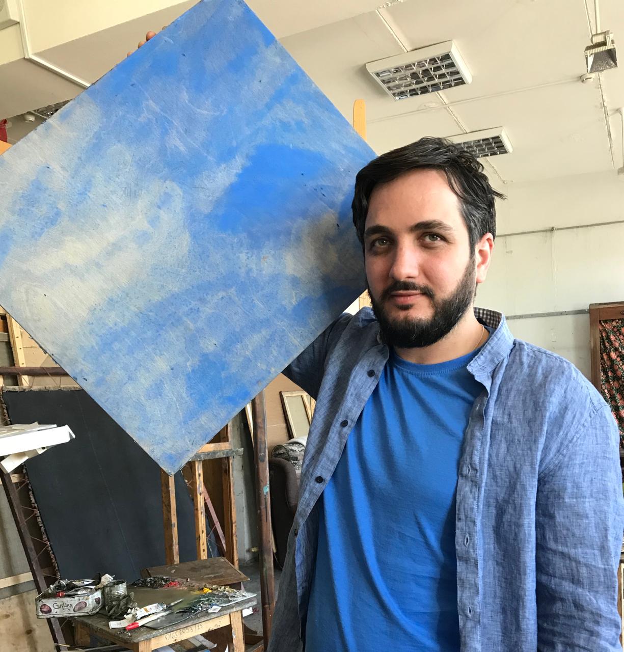 Zaza Khukhua in his painting studio, holding a blue canvas