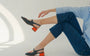 A woman seated on the floor wearing HUHUA navy slingbacks with sculpted red block heels
