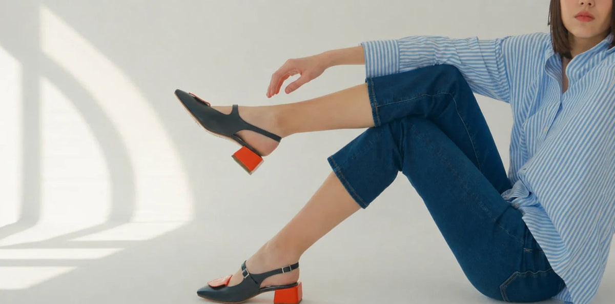 A woman seated on the floor wearing HUHUA navy slingbacks with sculpted red block heels